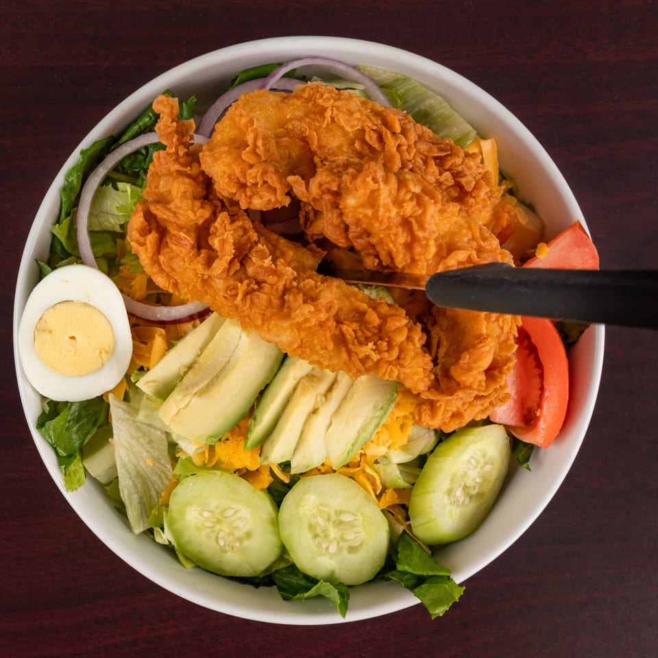 Crispy fried chicken salad with lettuce, avocado, cucumber, tomato, onion, cheese, and a hard-boiled egg.
