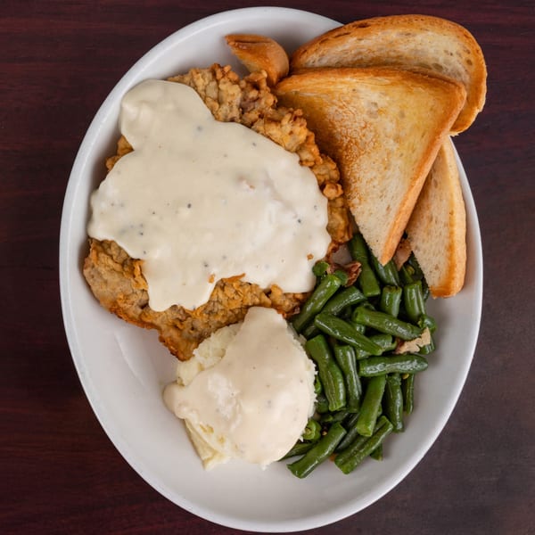 Chicken fried steak with gravy, mashed potatoes, green beans, and toast on a white plate.